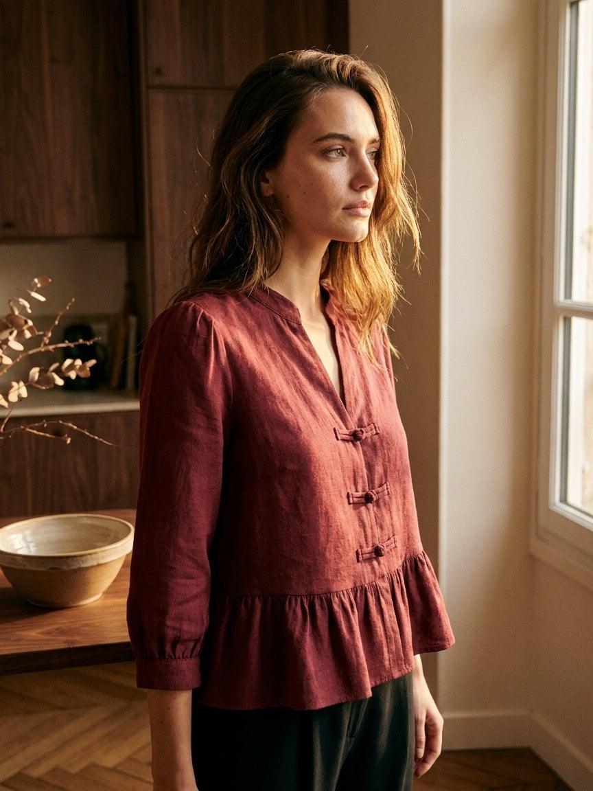 Femme en blouse Emilie bordeaux Ycoo à boutons brandebourgs, de profil près d'une fenêtre